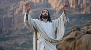 A photo of Jesus rising from the dead with his hands raised. He is wearing a white robe. The background is a mountainous area with rocks. The lighting is soft. He is risen.